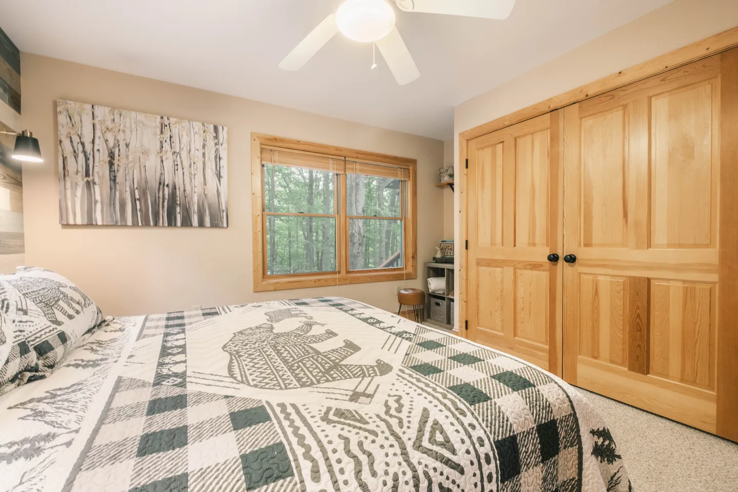 Bedroom with a patterned bear-motif bedspread, double wood closet doors, and a window framing forest views.