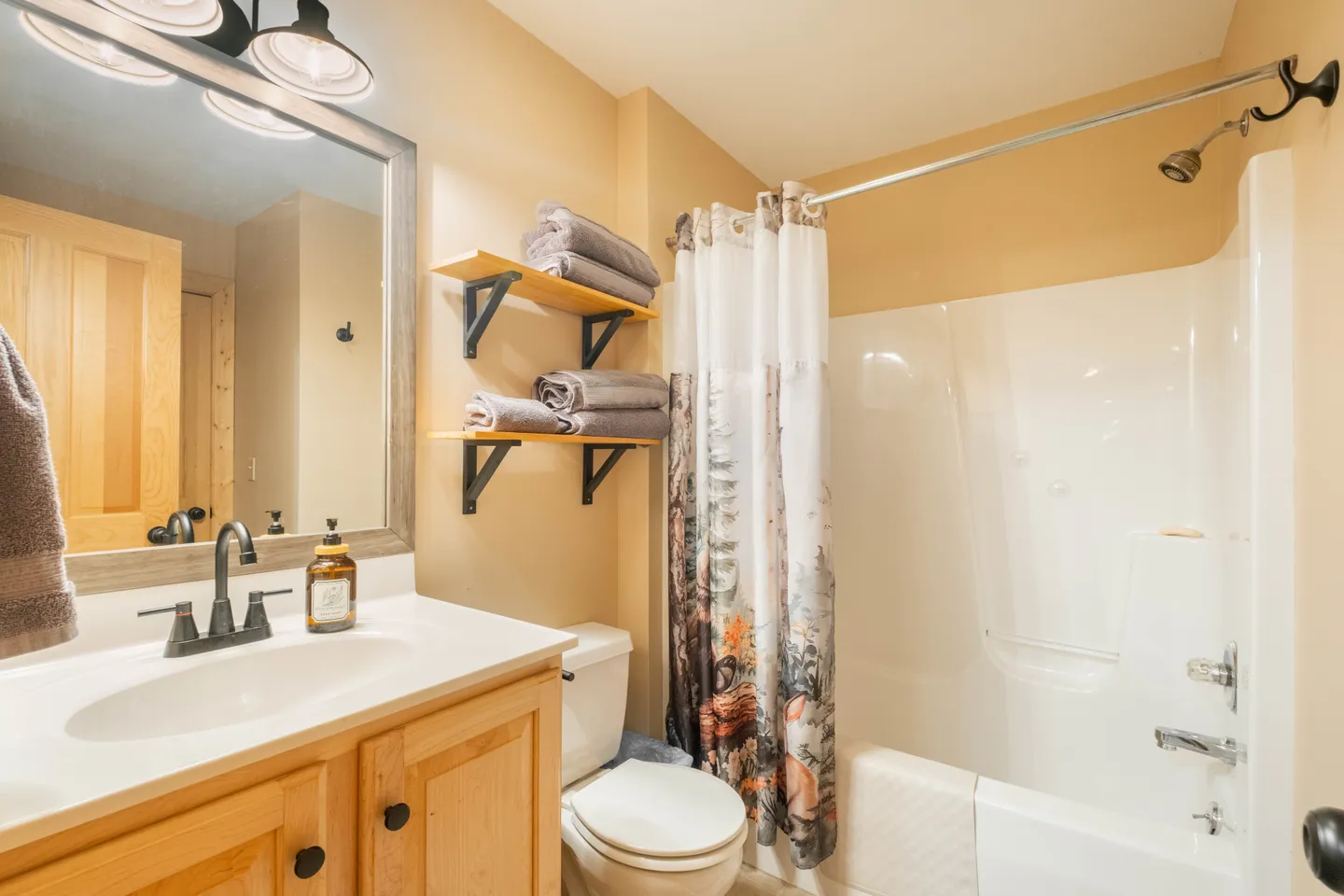 Bathroom with a light wood vanity, toilet, and shower-tub combination featuring a patterned shower curtain.