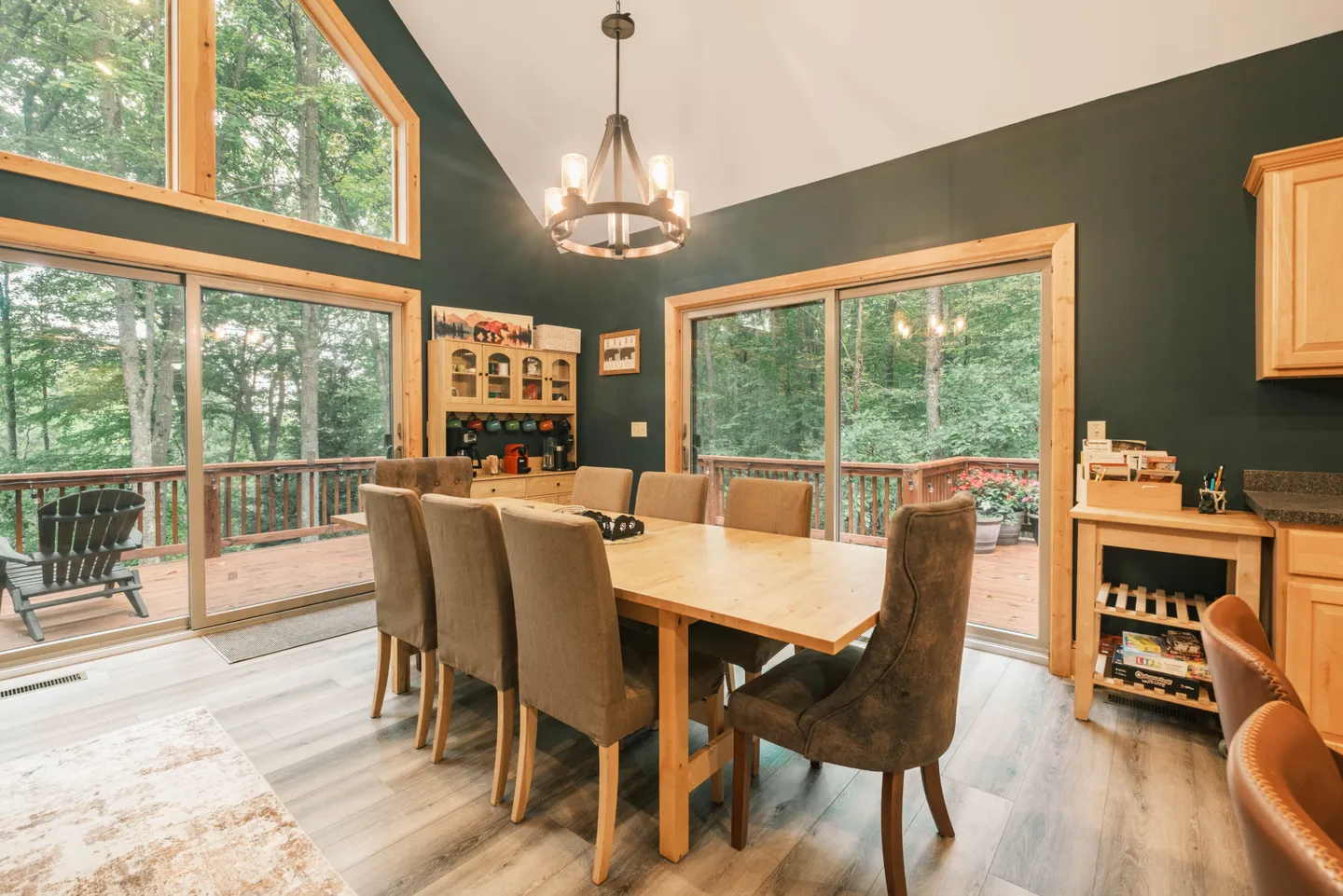 Dining area with a wooden table, upholstered chairs, sliding glass doors to a deck, and vaulted ceilings.