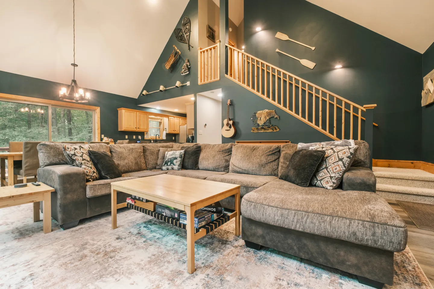 Living room with a large sectional sofa, coffee table, vaulted ceiling, and stairs leading to an upper level.
