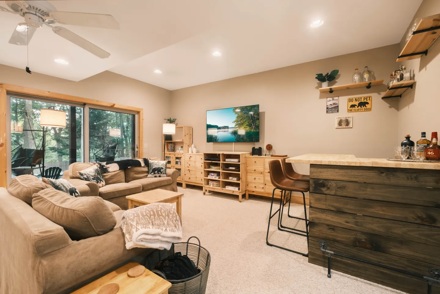 Living room and bar area with sofas, mounted TV, light wood shelving, and a wooden counter with bar stools.