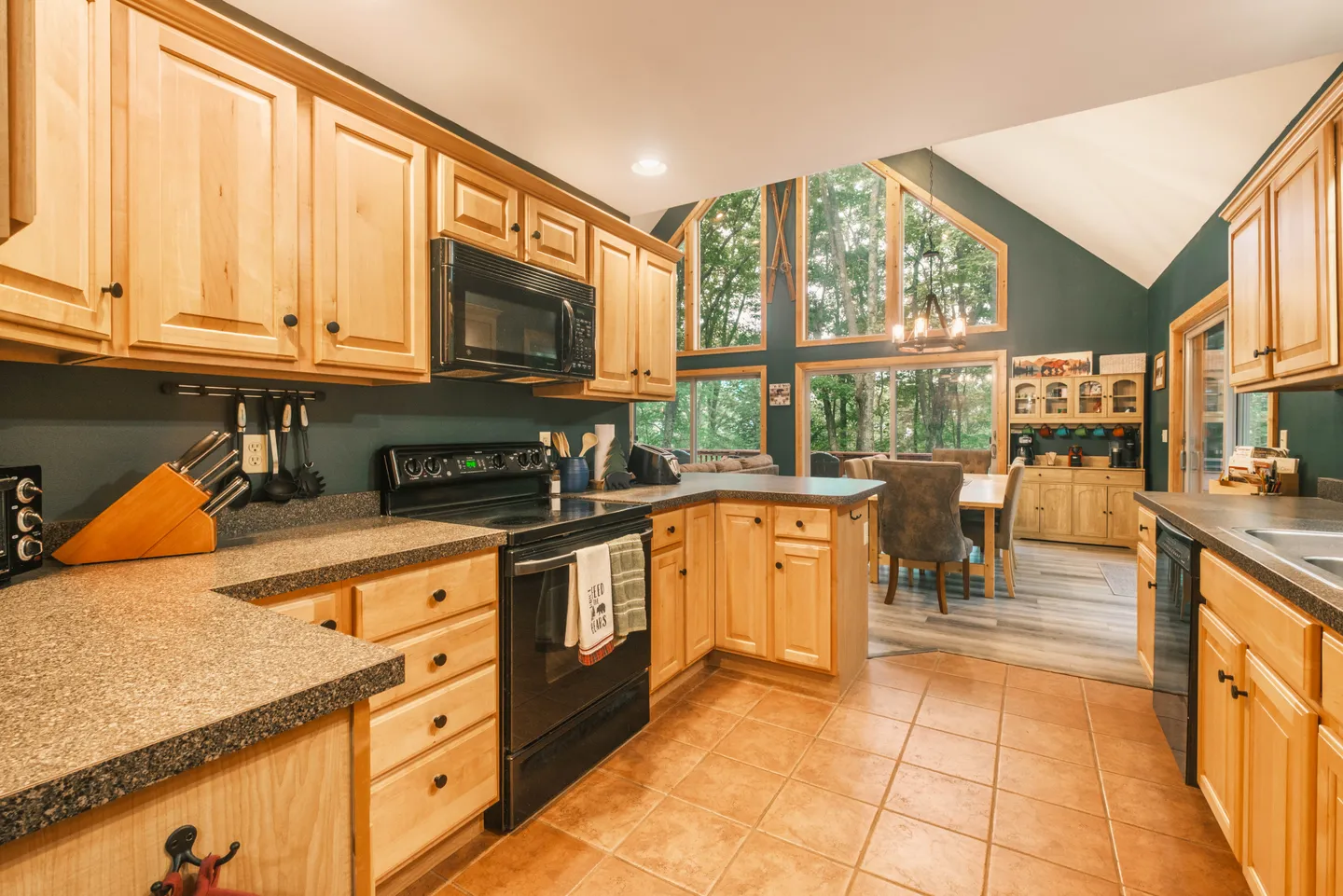 Kitchen with light wood cabinets and tiled floor looking toward an open dining room with tall pointed windows.