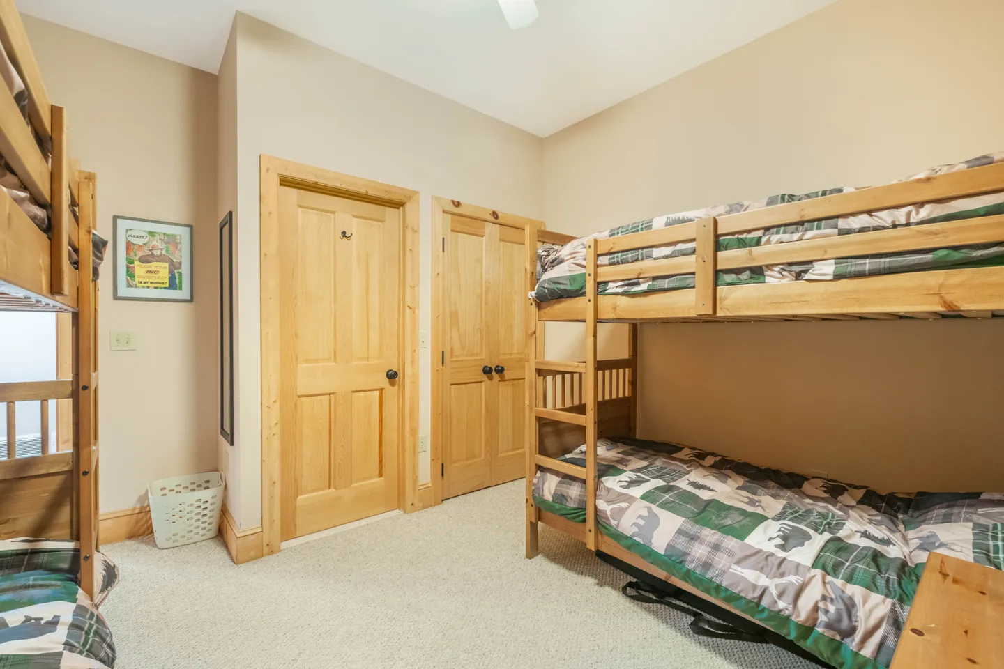 Bedroom featuring wooden bunk beds with patterned bedding, carpeted flooring, and light wood interior doors.
