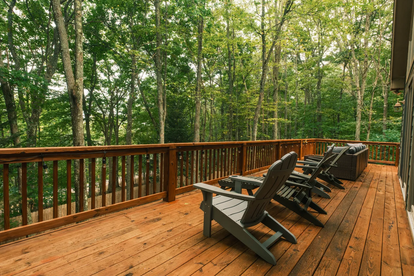 Spacious elevated wooden deck with Adirondack chairs overlooking a dense green forest.