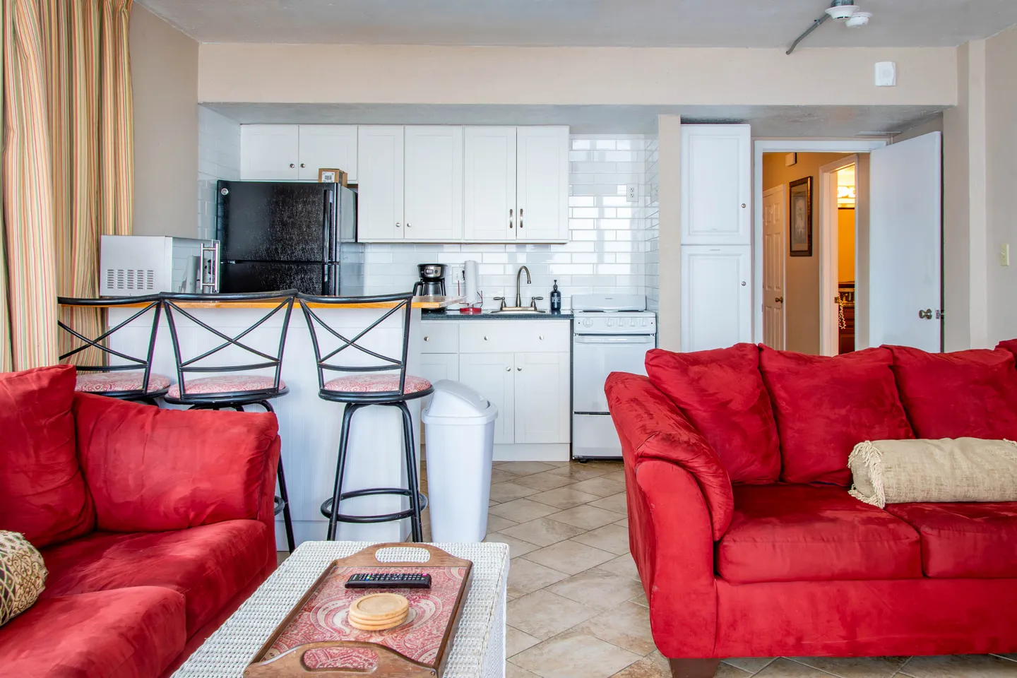 Open living area with red armchairs facing a kitchen with white cabinetry and breakfast bar seating.