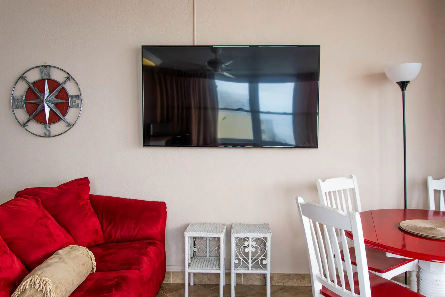 Living area featuring a wall-mounted flat-screen television, a red sofa, a compass rose wall decoration, and a red dining table with white chairs.