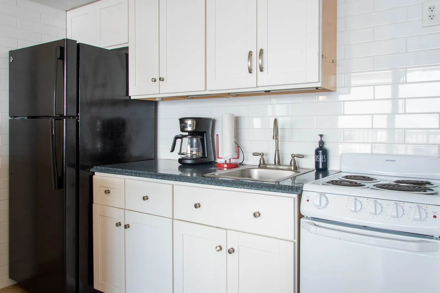 A compact kitchen featuring white shaker cabinets, a black refrigerator, a white electric range, and a subway tile backsplash.