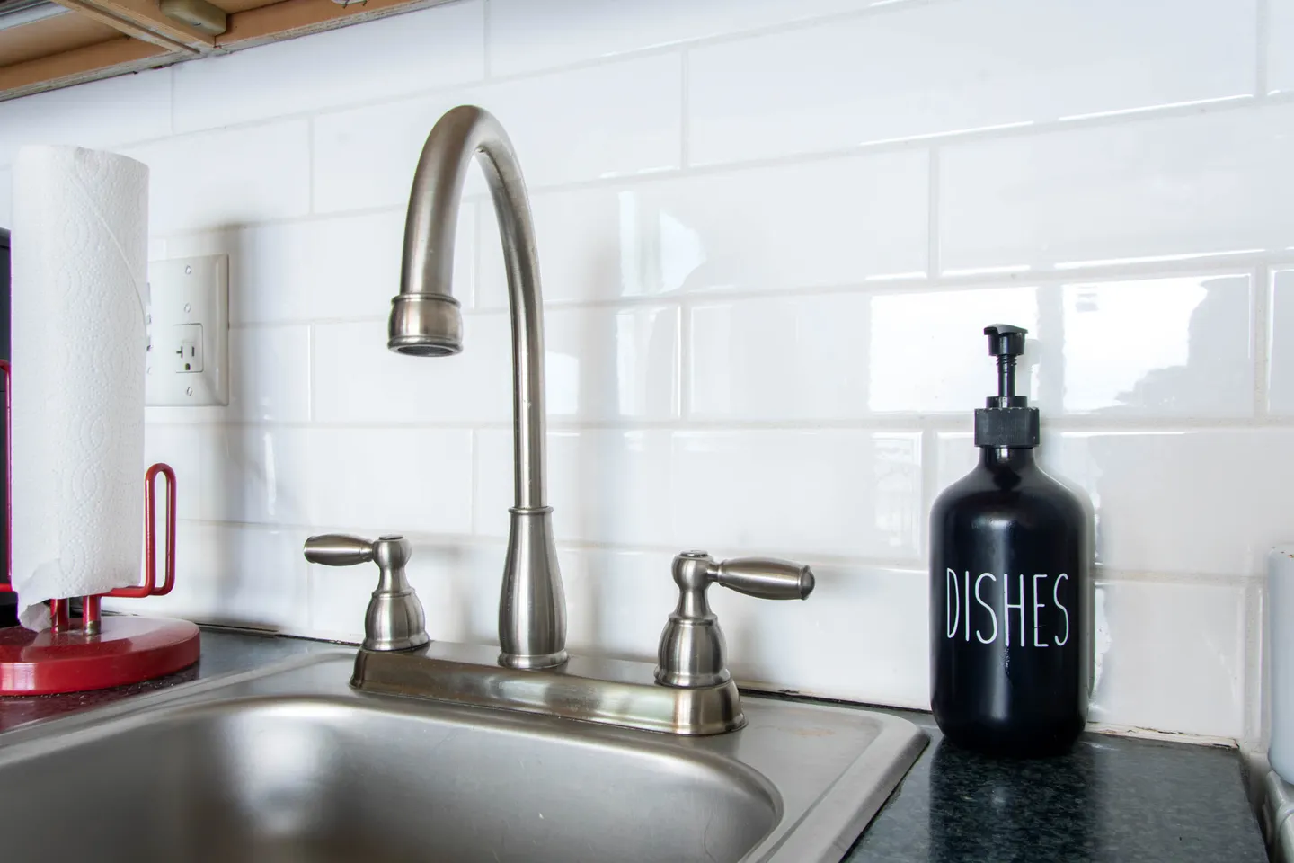 Close-up of a brushed metal kitchen faucet and sink set against a white subway tile backsplash.