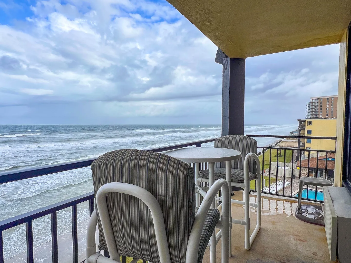 Covered balcony with high-top table and chairs overlooking the ocean and coastline.