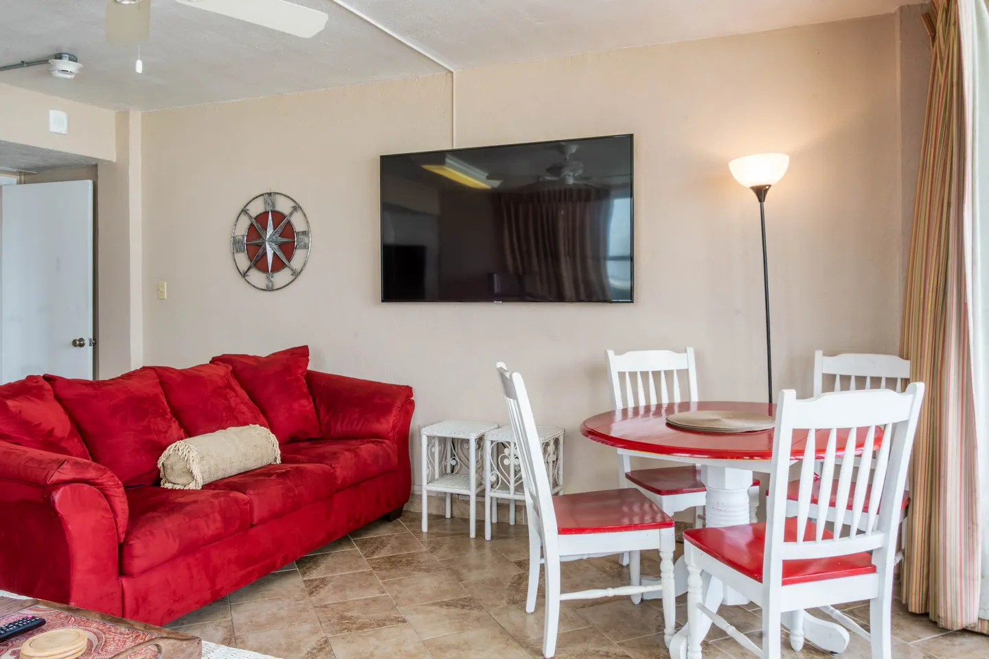 Living area featuring a bright red sofa, tiled floors, a wall-mounted flat-screen television, and a round dining table with white and red chairs.