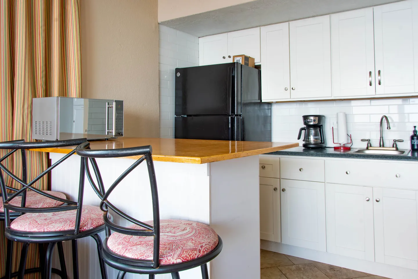 Kitchen area featuring white cabinets, a breakfast bar with metal barstools, a black refrigerator, and a microwave.