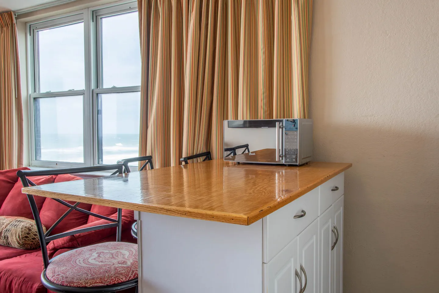 A kitchen island with a light wood countertop, a stainless steel microwave, and bar seating next to a window showing ocean views.