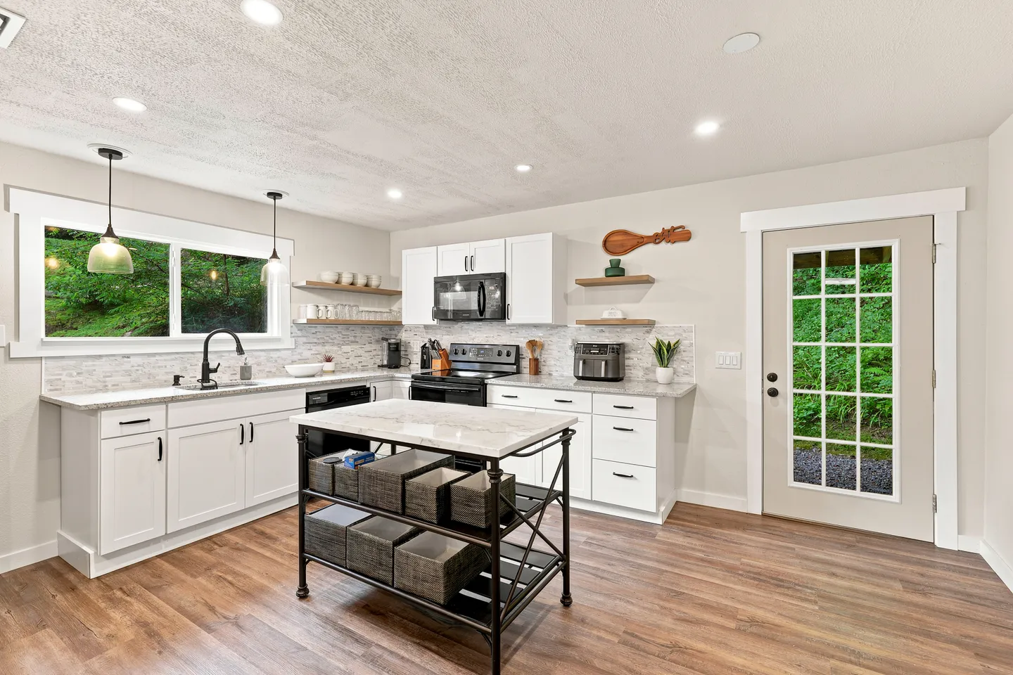 Bright kitchen featuring white shaker cabinets, light countertops, wood-style flooring, a central mobile island, and an exterior door with glass panes.