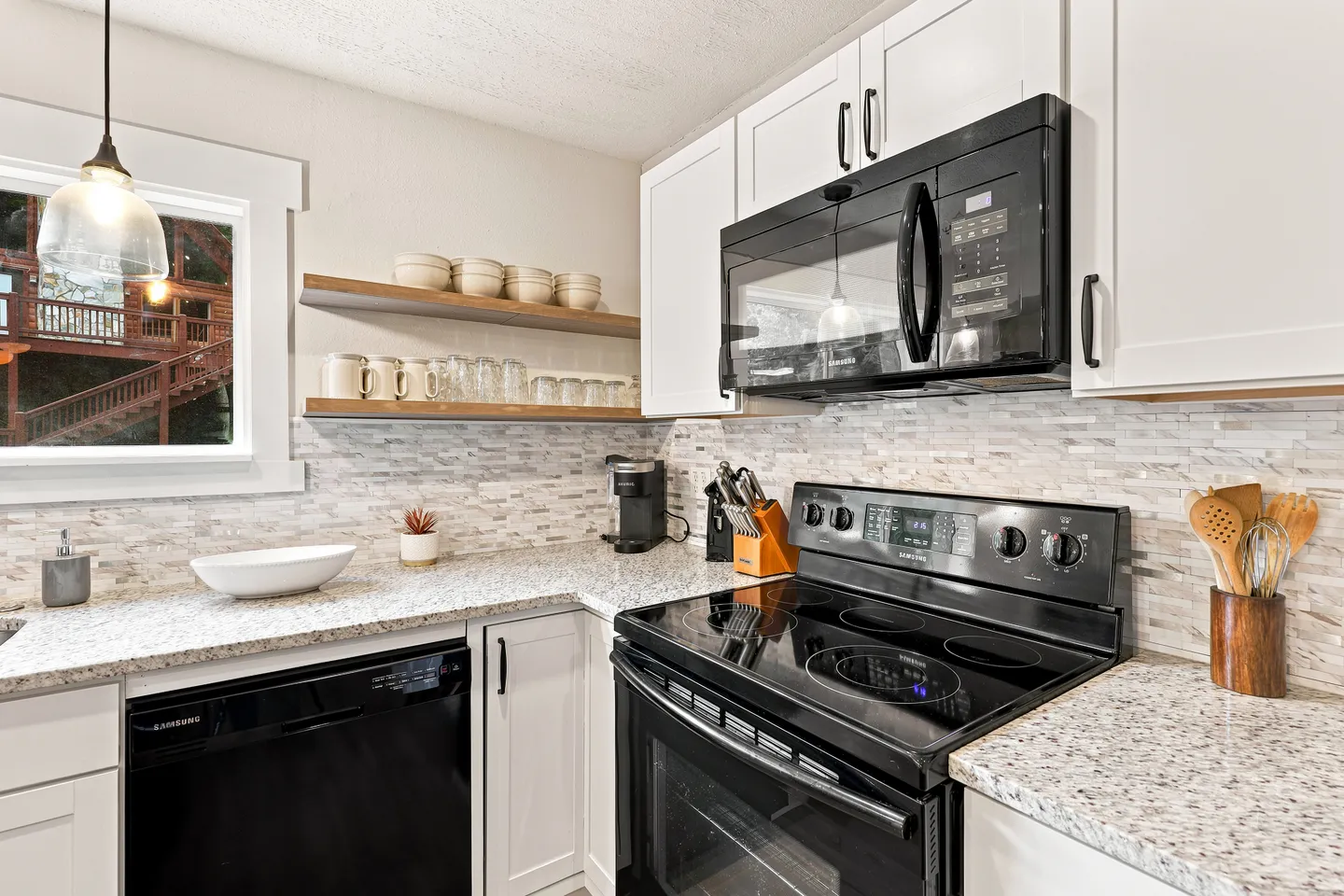 Close-up view of a kitchen corner featuring white shaker cabinets, speckled countertops, a black electric range, and open floating wooden shelves.