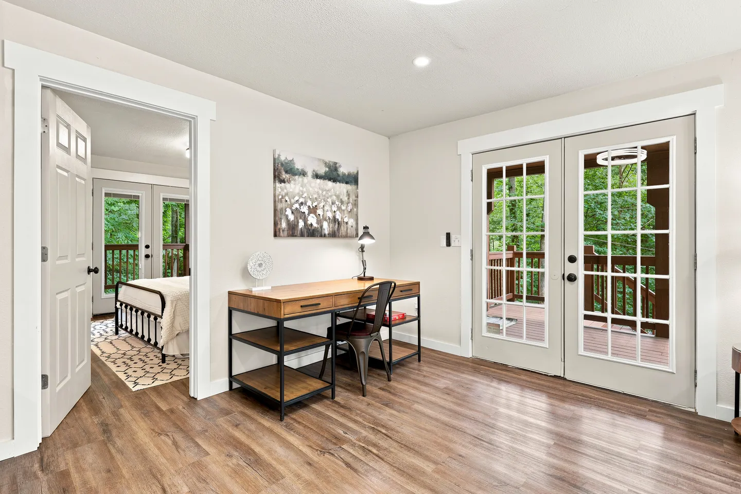 Workspace area with a wooden desk and chair, French doors leading to an exterior deck, and an open doorway showing an adjacent bedroom.