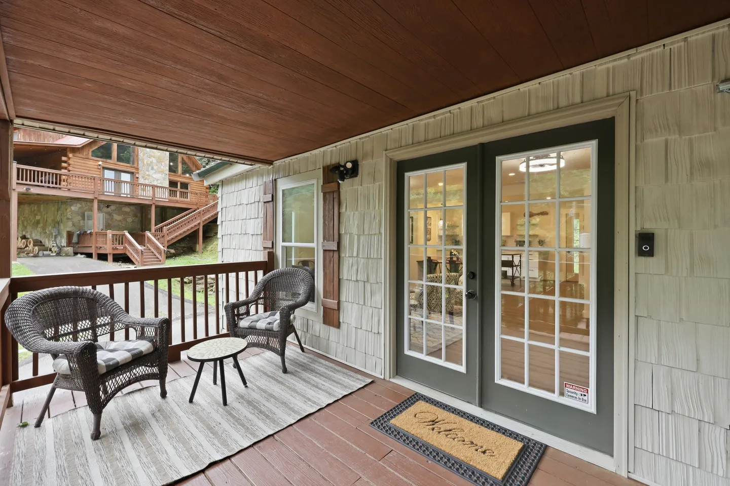 Covered porch featuring two wicker armchairs, a small side table on an outdoor rug, and French glass doors leading inside.