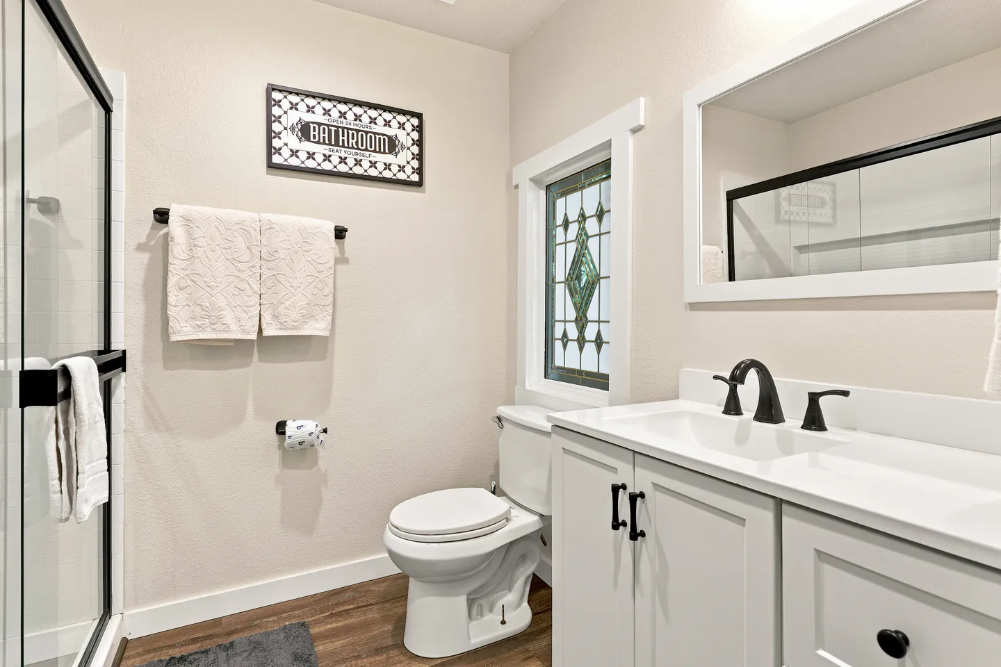 Bathroom with white vanity, toilet, decorative stained glass window, and glass shower door.