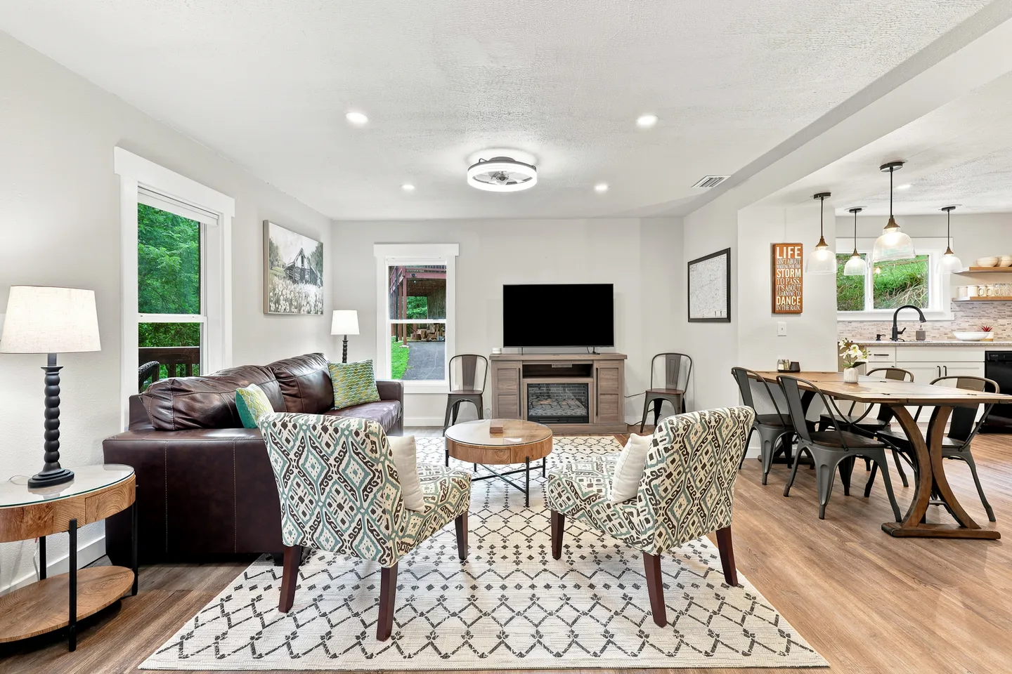 Open-concept living room and dining area featuring a brown leather couch, patterned armchairs, television, and adjacent wooden dining table.