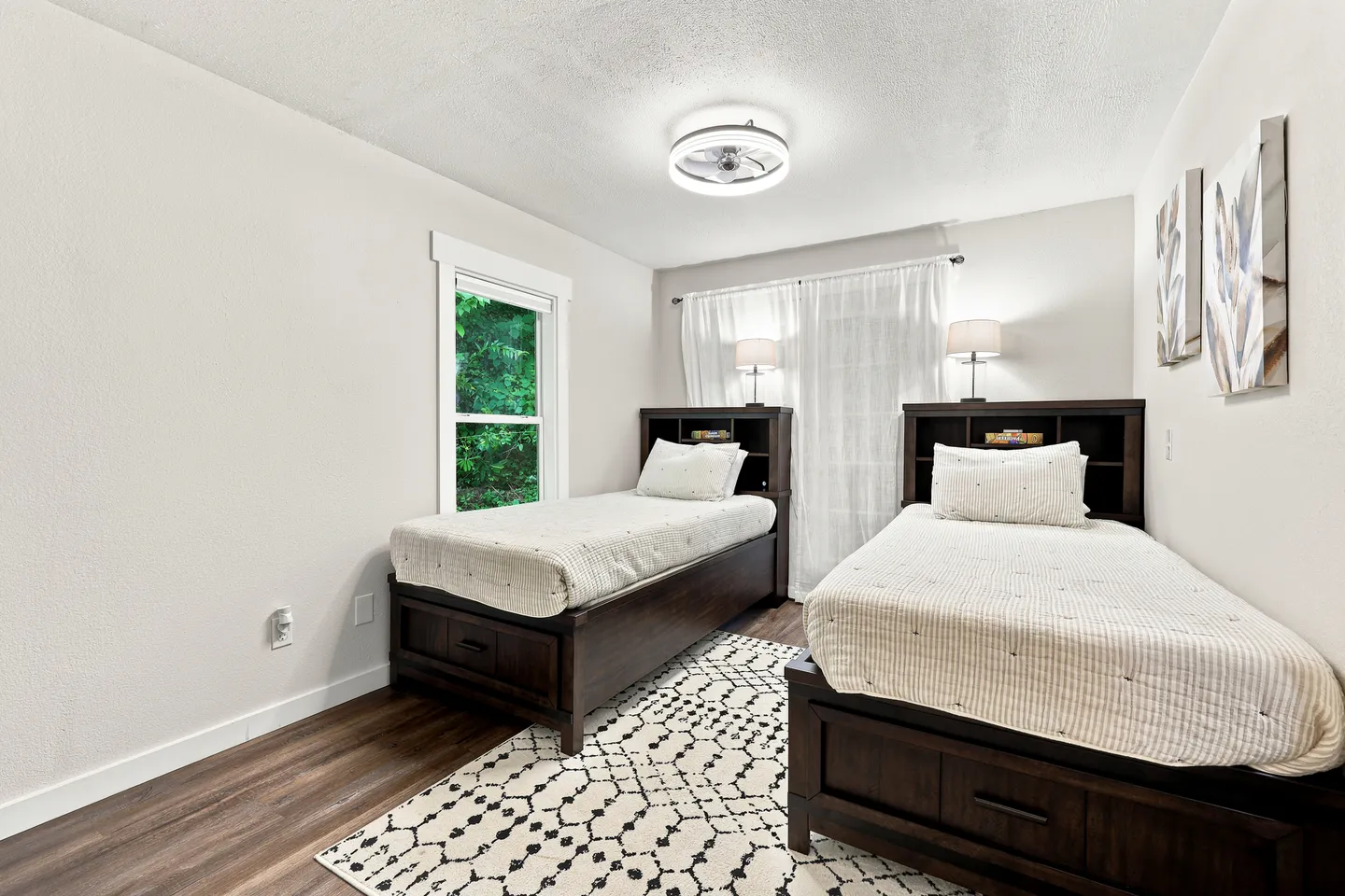 Bedroom with two dark wood twin beds, white bedding, bookcase headboards, and a patterned area rug over wood-look flooring.