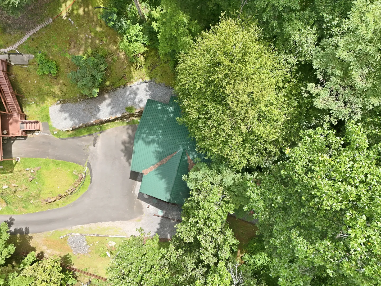 Overhead aerial view of a green-roofed detached structure, paved driveway, and surrounding dense forest trees.