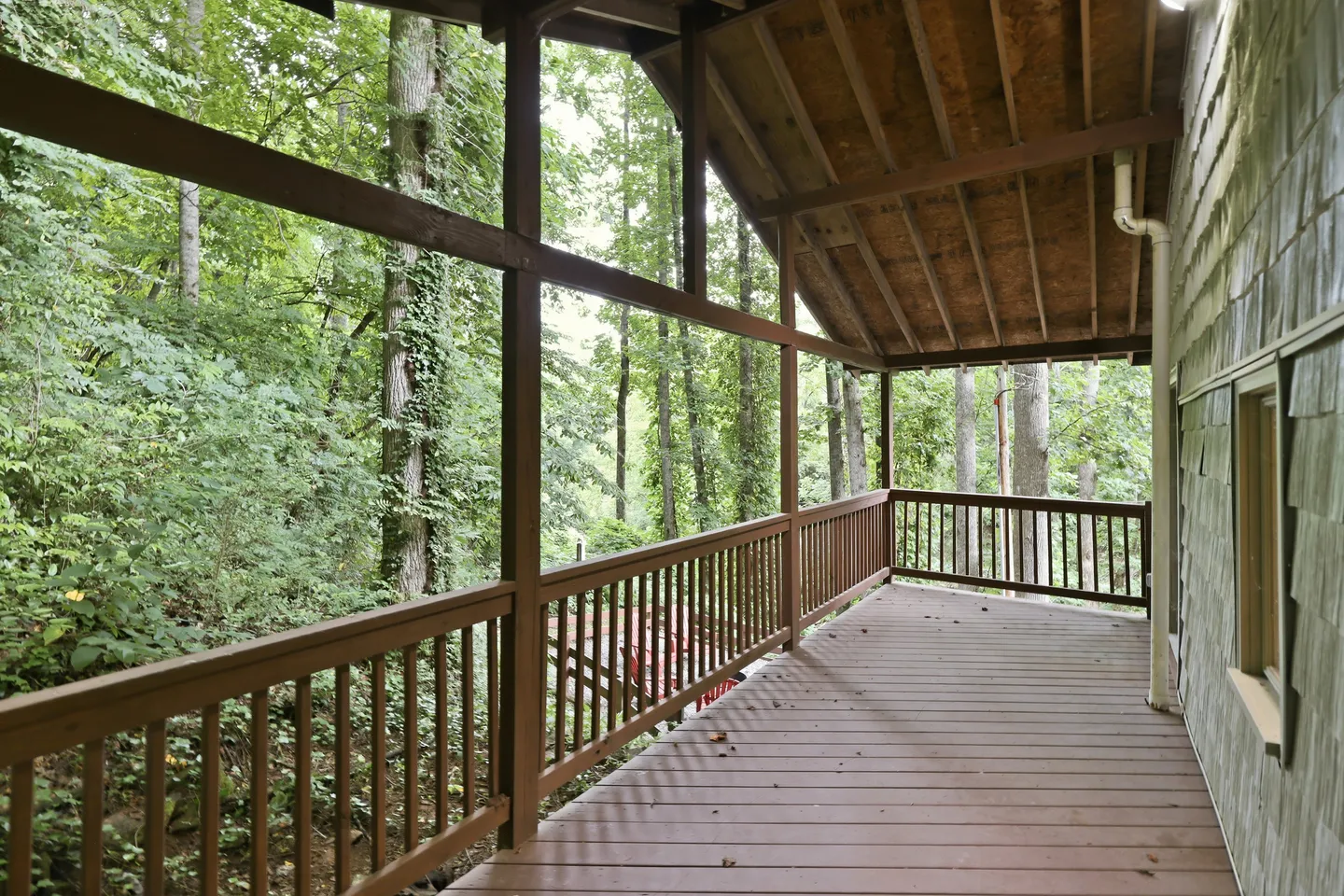 A covered wooden deck with railings overlooking a dense forest of green trees.