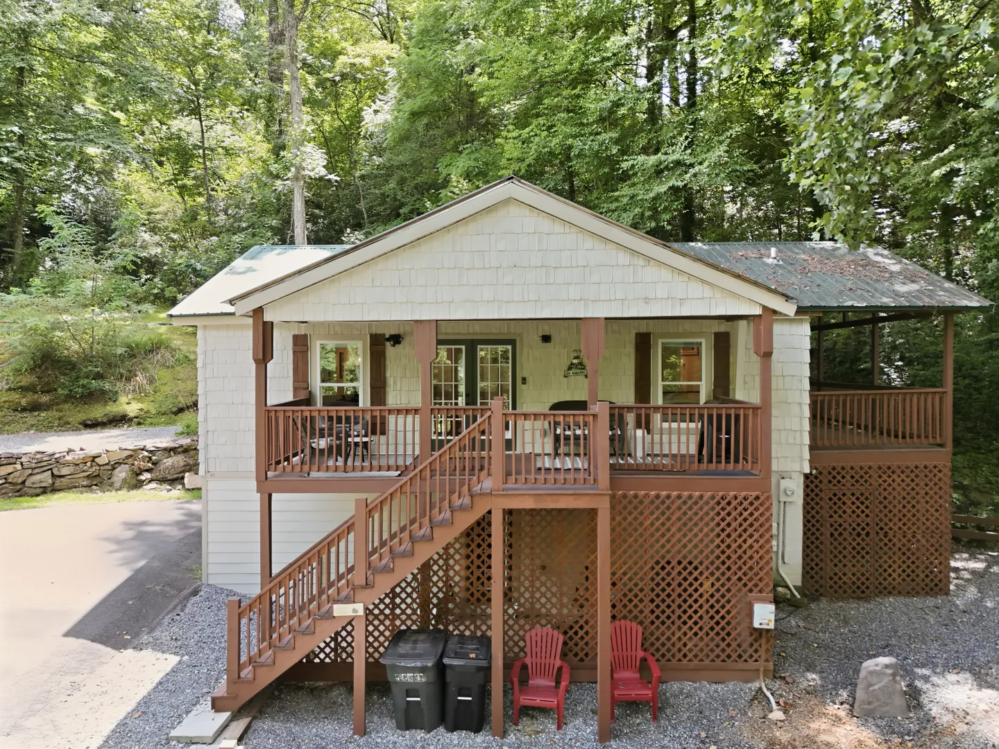 Exterior front view of an elevated cabin surrounded by woods, featuring a covered wooden porch with an exterior staircase.
