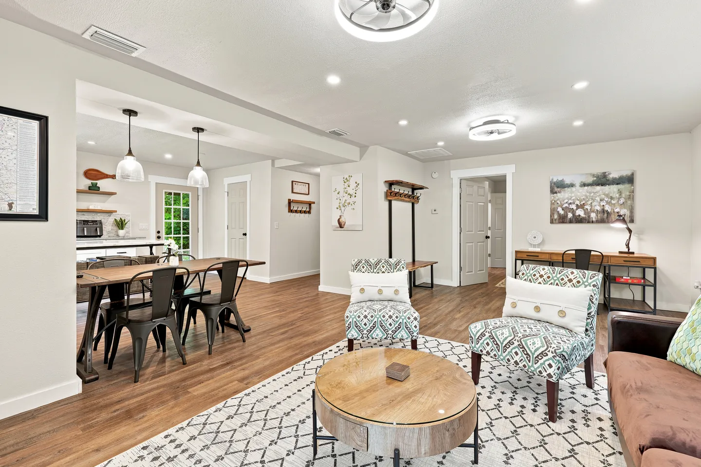 Open-concept living room with patterned accent chairs, dining table with metal chairs, and wood-look flooring.