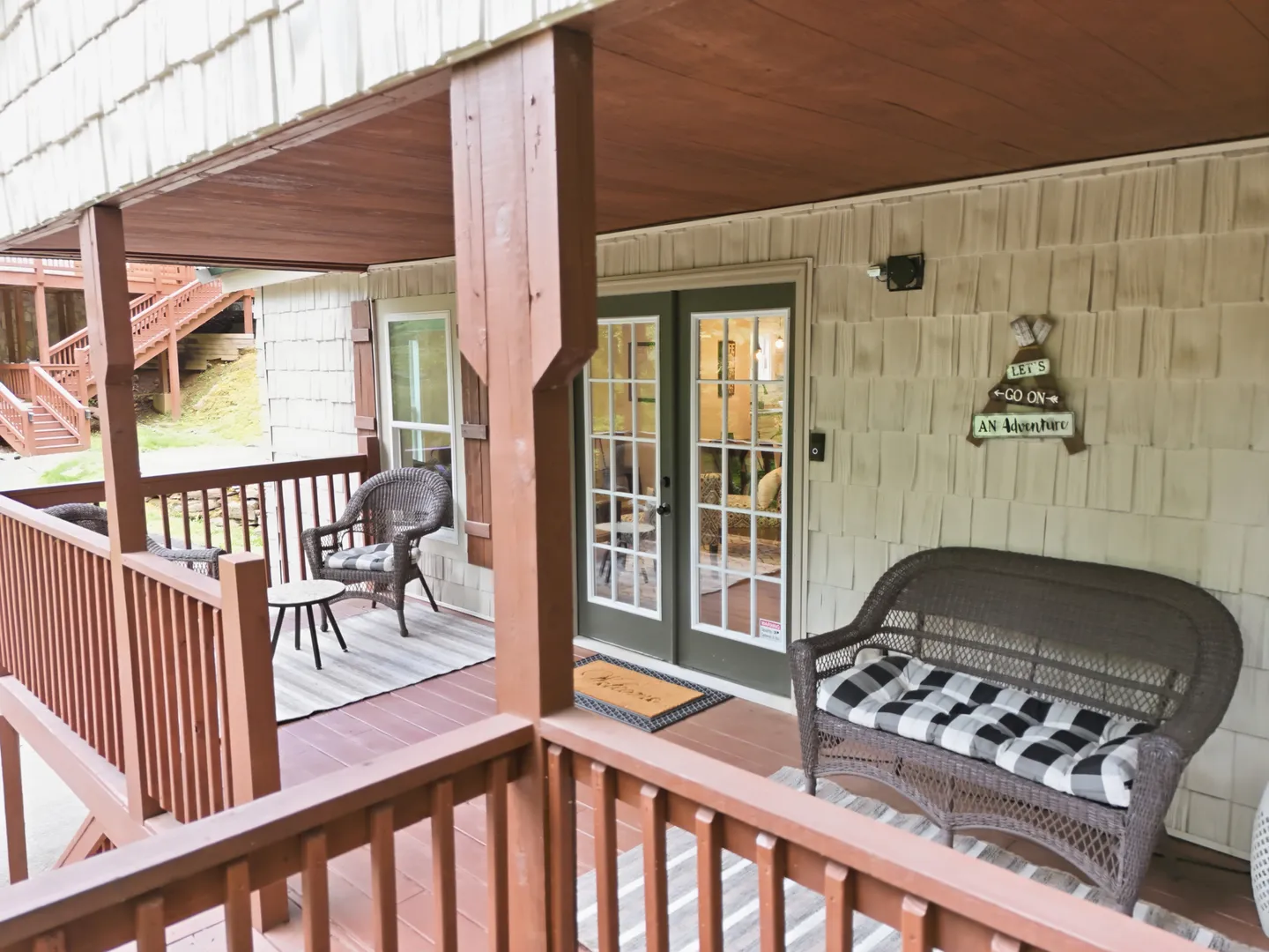 Covered outdoor porch with wicker seating, french doors, and wood railings.
