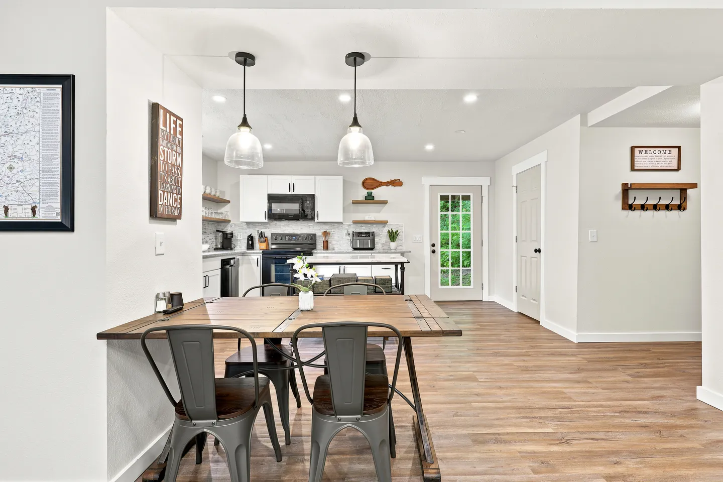 Dining area with wood-topped table and metal chairs looking into an open kitchen with white cabinets.