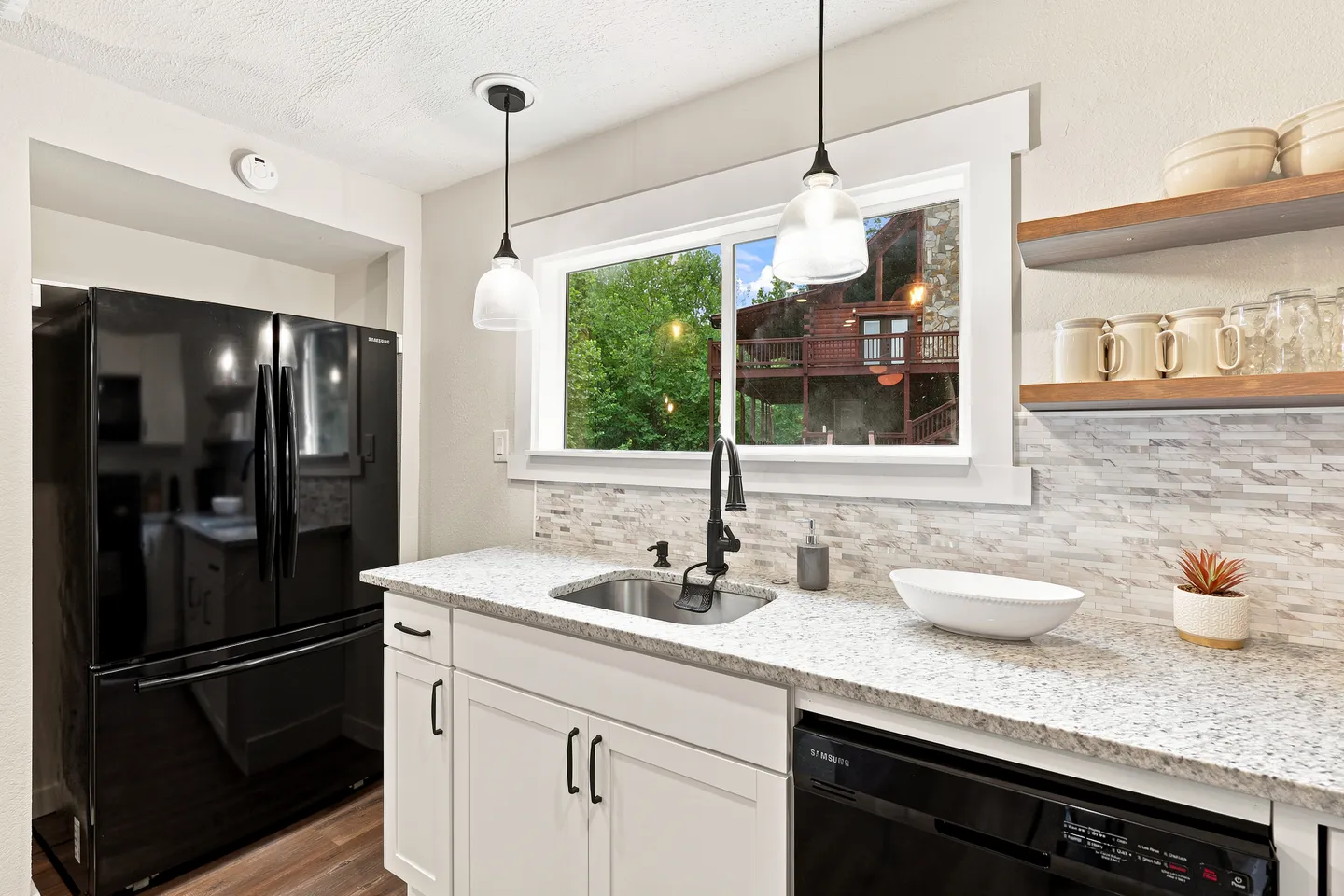 Kitchen counter with an undermount sink below a window looking out toward trees and a neighboring building.