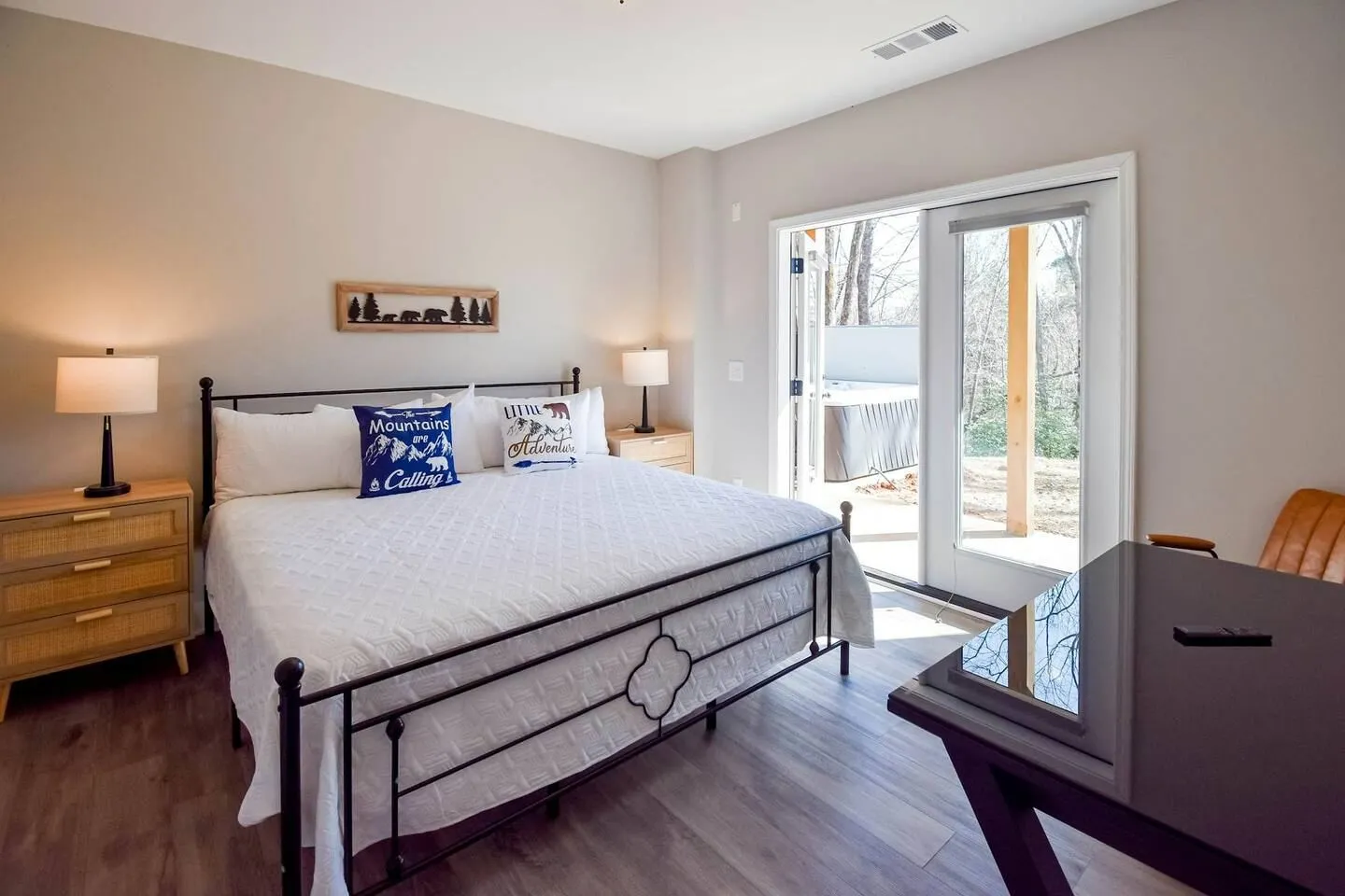 Bedroom with a large wrought iron frame bed, two nightstands with lamps, and glass doors opening to an outdoor patio with a hot tub.