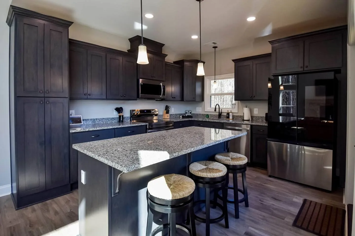 Kitchen with dark cabinetry, granite countertops, an island with three stools, and stainless steel appliances.