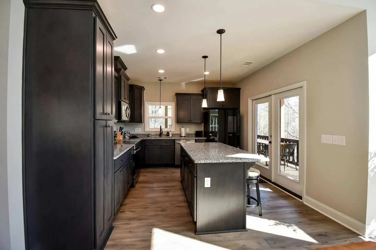 Kitchen with dark cabinetry, granite-style countertops, an island with bar seating, and glass doors leading outside.