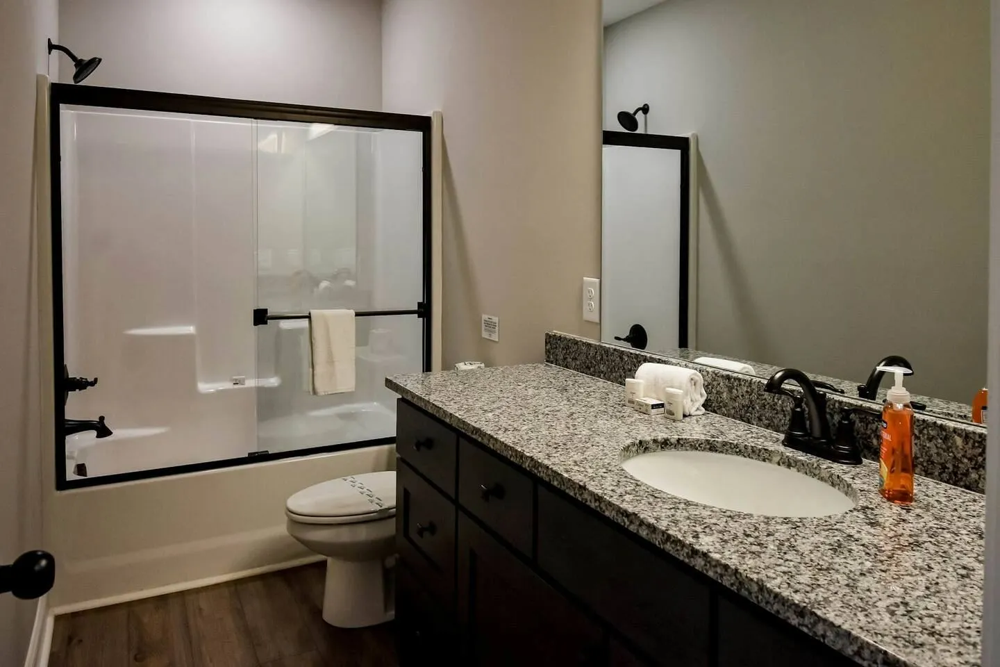 Bathroom with granite vanity countertop, mirror, toilet, and shower-tub combination with sliding glass doors.