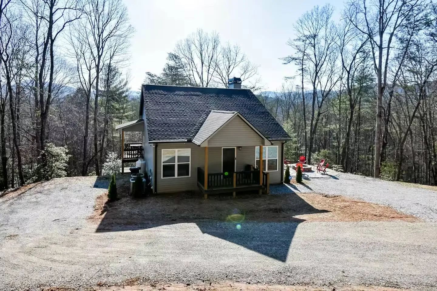 Exterior view of a cabin with a covered front porch and gravel driveway surrounded by trees.