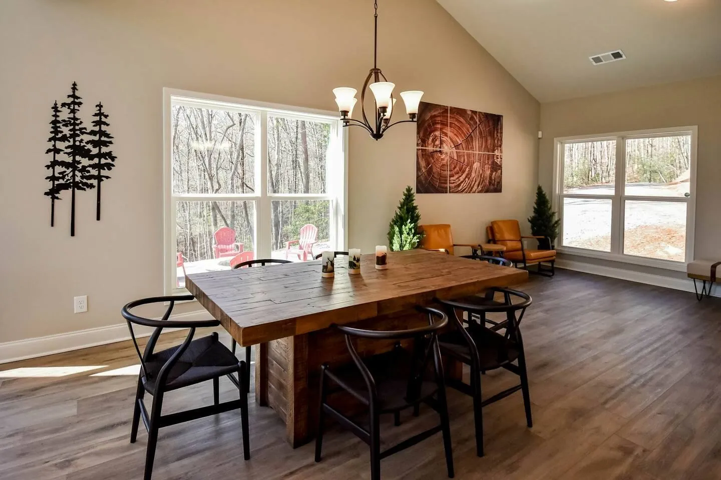 Dining area with a wooden table, black curved chairs, hanging light fixture, and windows showing trees outside.