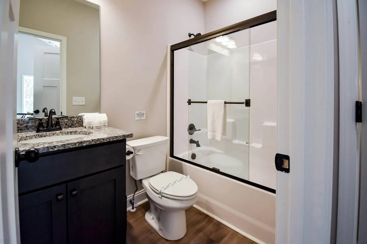 Bathroom with dark vanity, speckled countertop, white toilet, and a shower-tub combo behind sliding glass doors.