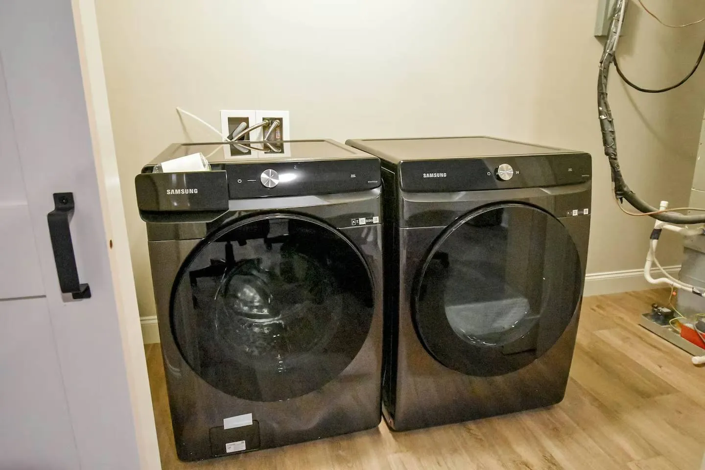 A matching dark gray front-loading washer and dryer set sitting side-by-side on light wood-look flooring.