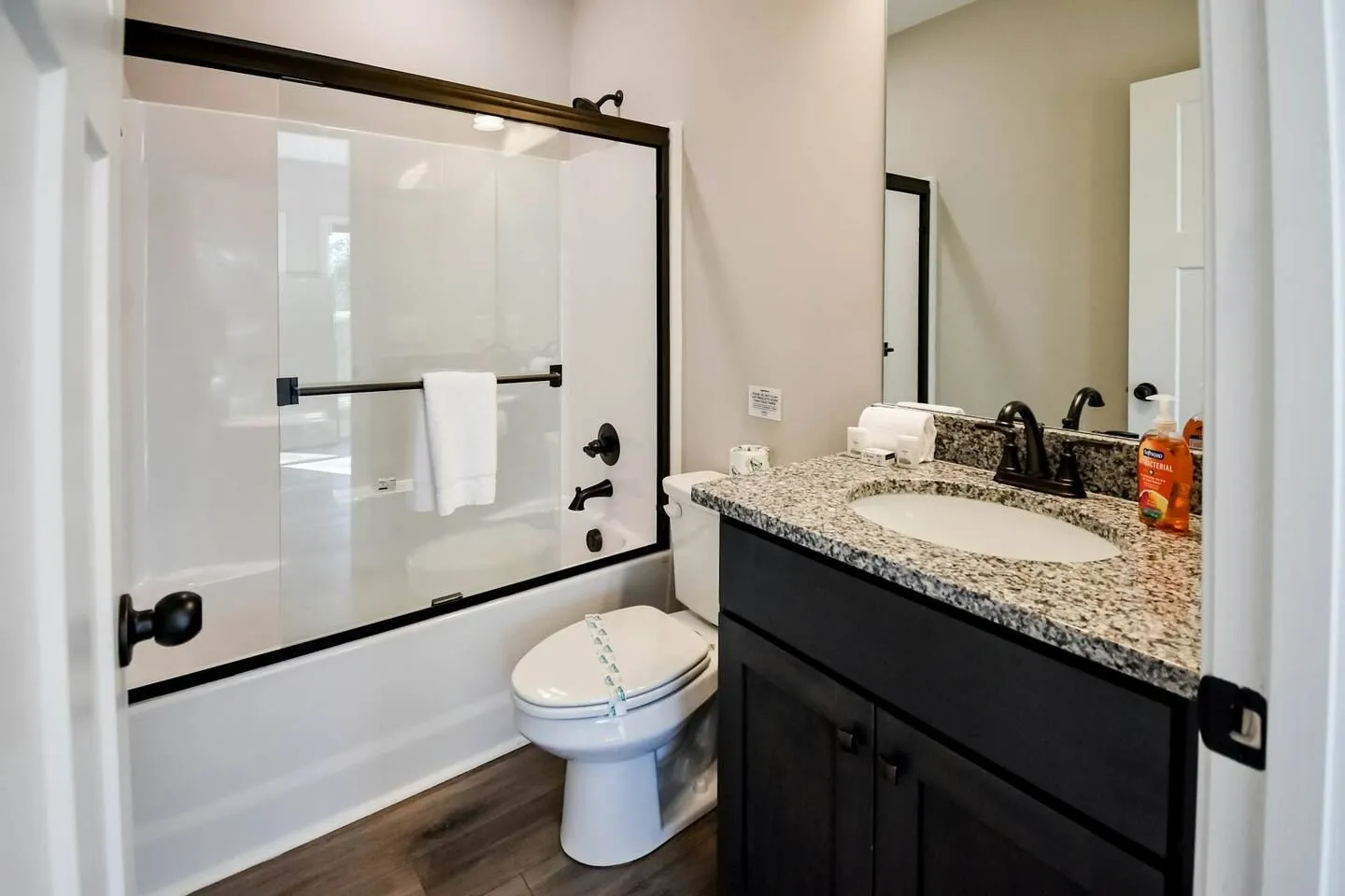 Bathroom with dark wood vanity, speckled countertop, toilet, and a glass-enclosed bathtub and shower combination.