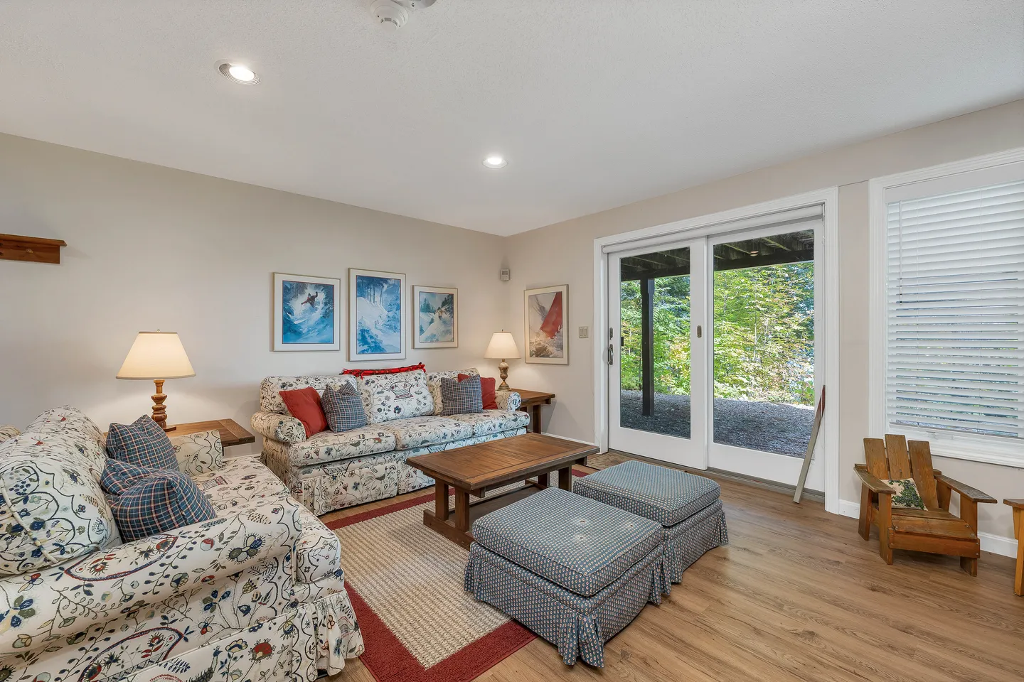 Living room with patterned floral couches, wood-laminate flooring, ski art on the wall, and sliding glass doors.