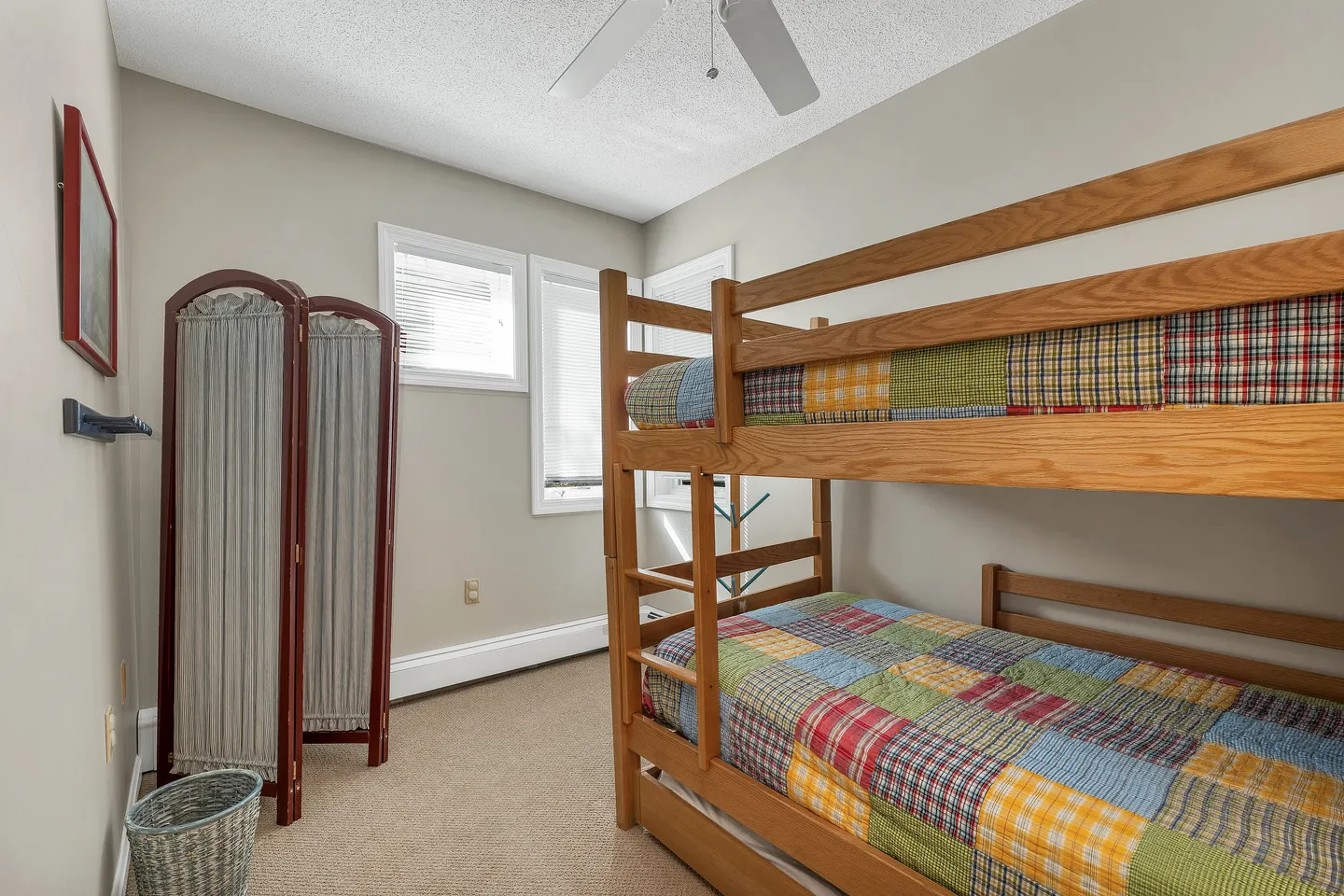 Bedroom with wooden bunk beds dressed in patchwork quilts, carpeted flooring, and a folding privacy screen.