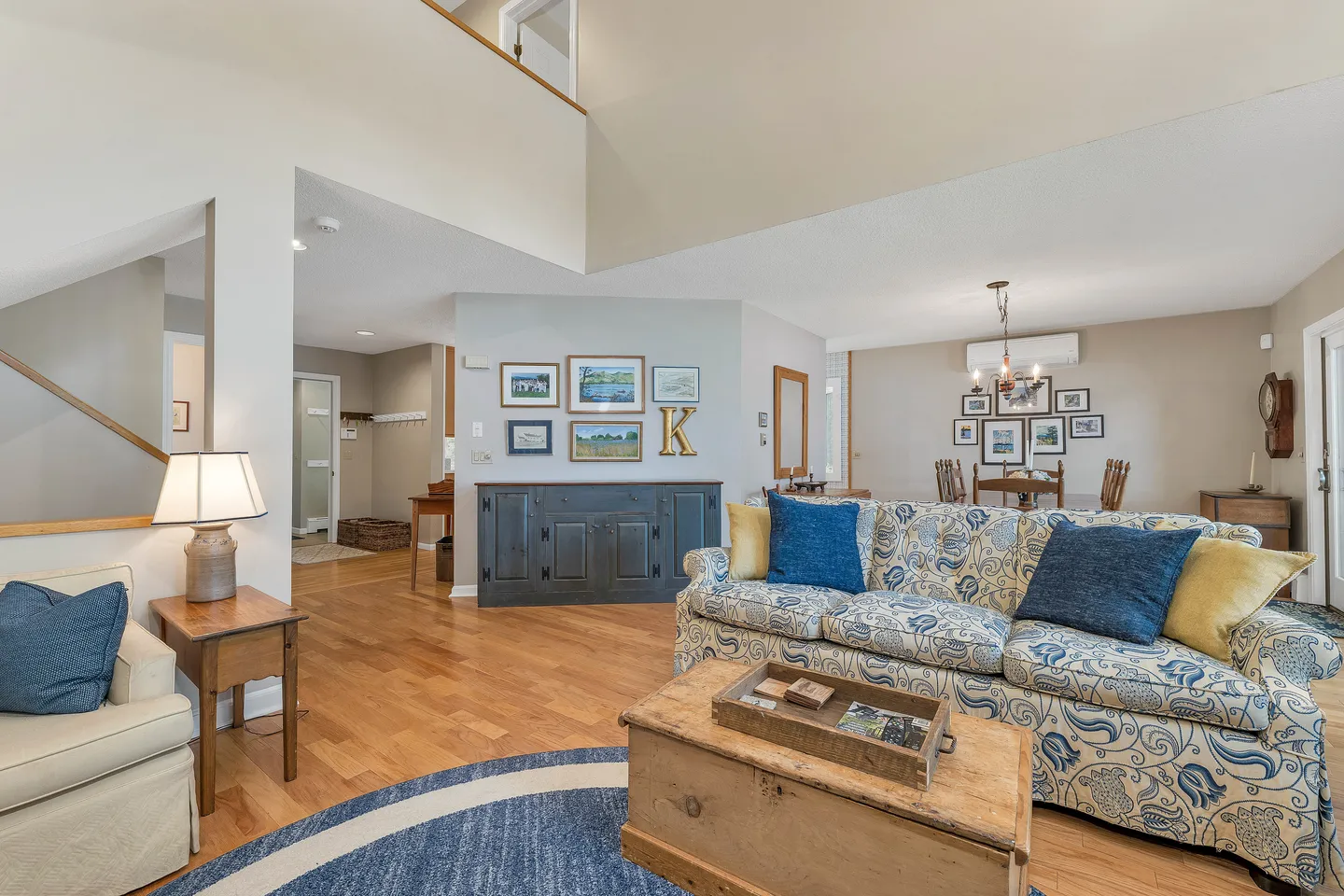 Open-concept living room with a patterned floral sofa, hardwood floors, and a view into the dining area and hallway.