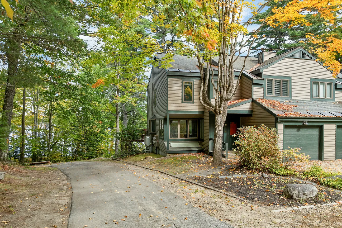 Exterior front view of a multi-level wood-sided townhome framed by autumn trees with a paved driveway.
