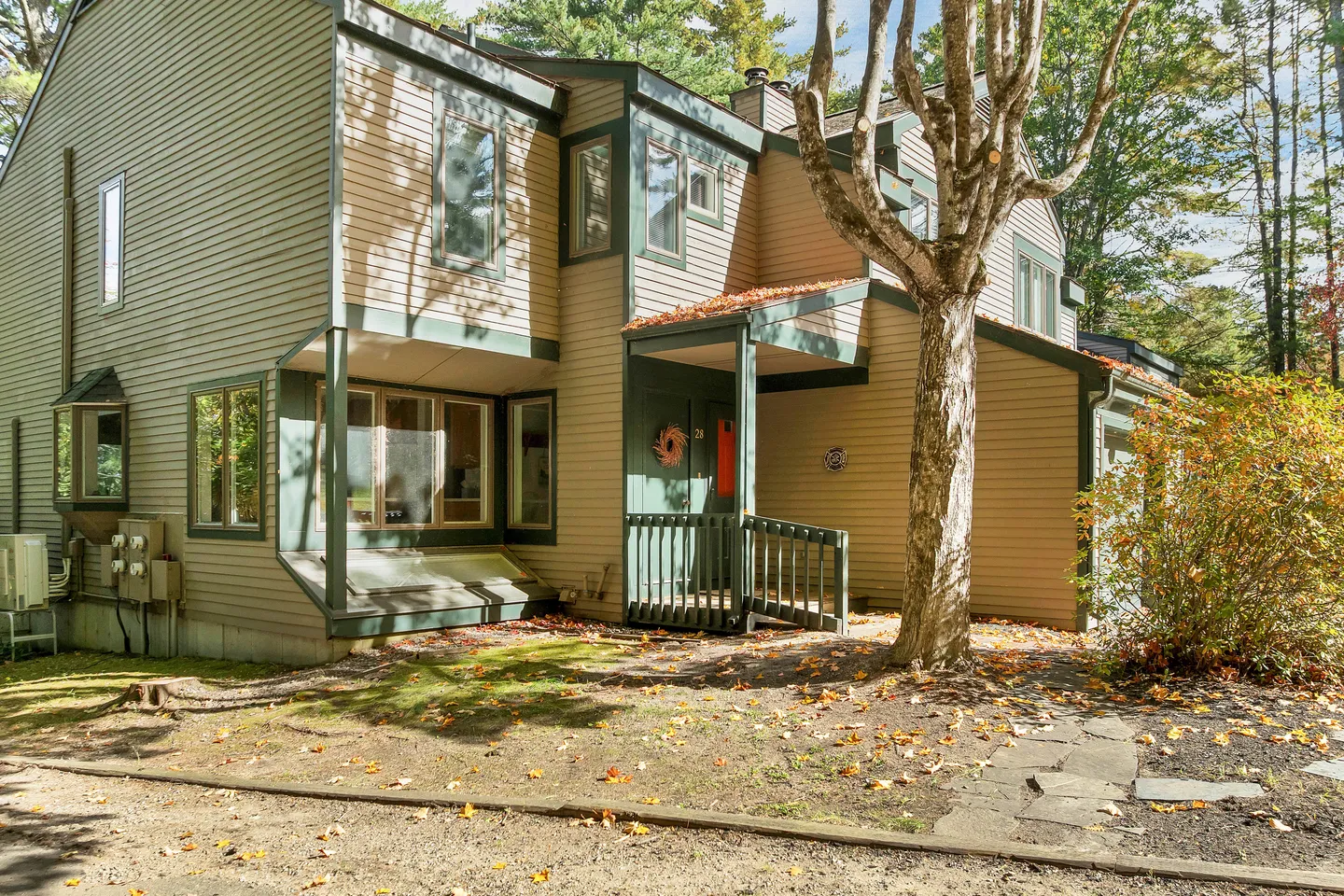 Exterior front view of a multi-story home with tan siding, dark green trim, and a small covered entryway nestled among trees.