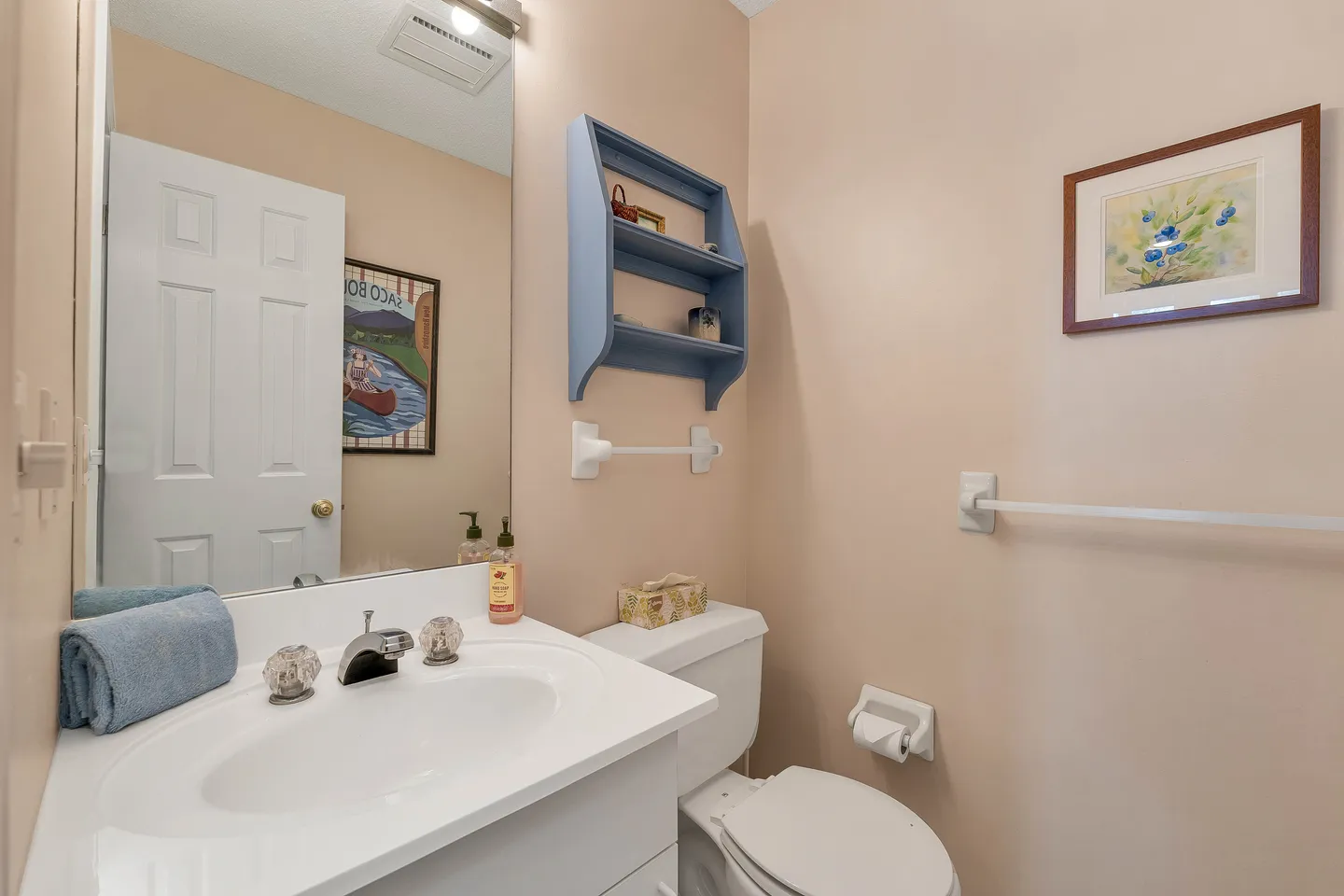Powder room with a white single vanity, oval sink, toilet, and light blue wall shelf.