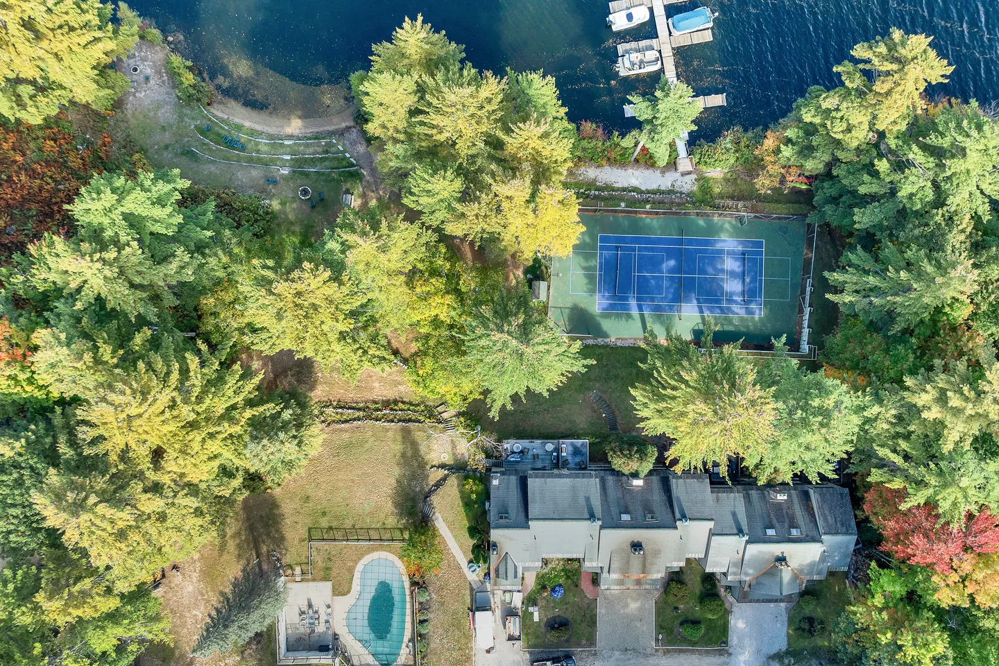 Aerial view of a lakefront estate featuring a large house, a swimming pool, a tennis court, and a boat dock.