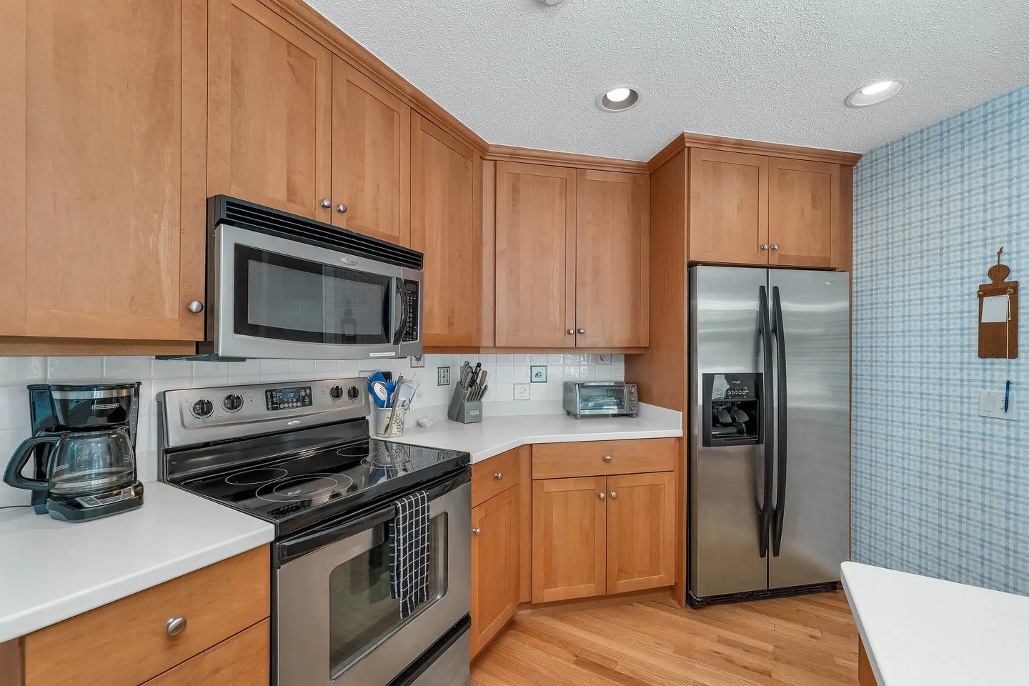 Kitchen with light wood cabinetry, white countertops, and stainless steel appliances including a refrigerator, stove, and microwave.