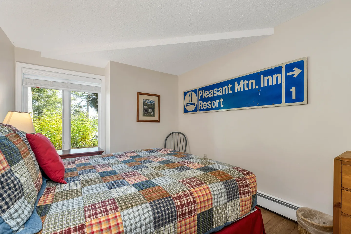 Bedroom with a patchwork quilt on the bed and a blue Pleasant Mountain Inn Resort road sign on the wall.