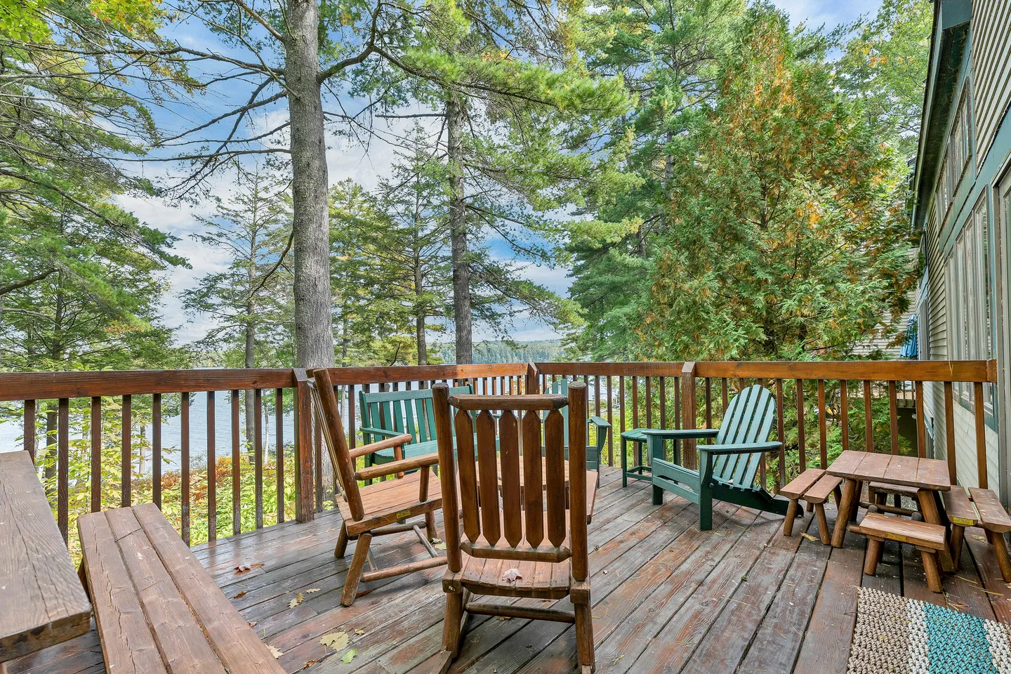 Wooden deck with outdoor chairs and benches surrounded by pine trees overlooking a lake.