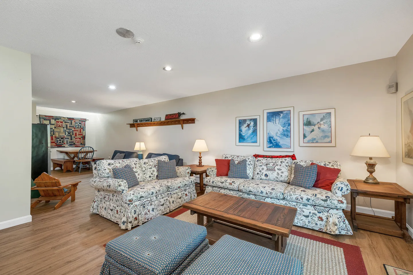 Living room with patterned floral couches, wood coffee table, ottomans, and recessed lighting.
